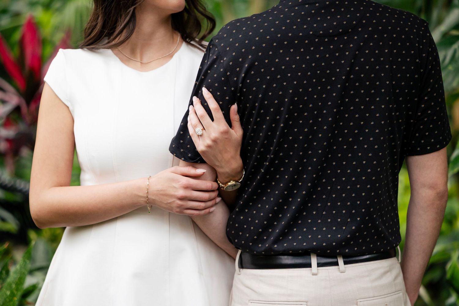 A couple embraces in a romantic garden setting surrounded by tropical plants and greenery.
