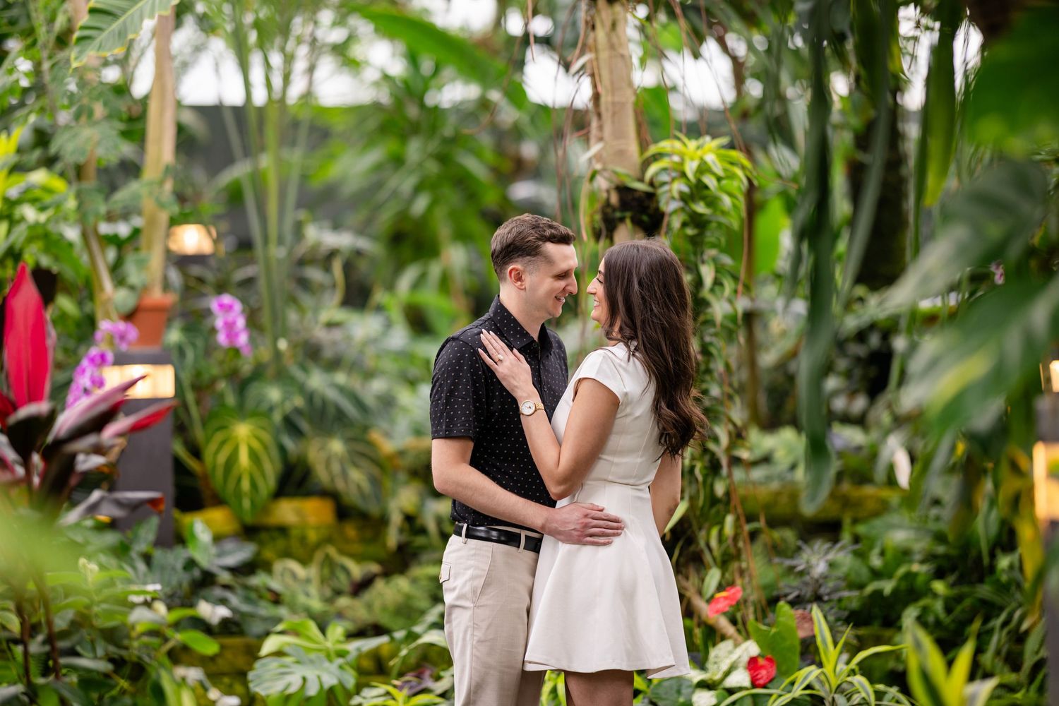A couple embracing on a garden path surrounded by vibrant tropical foliage and orchids.