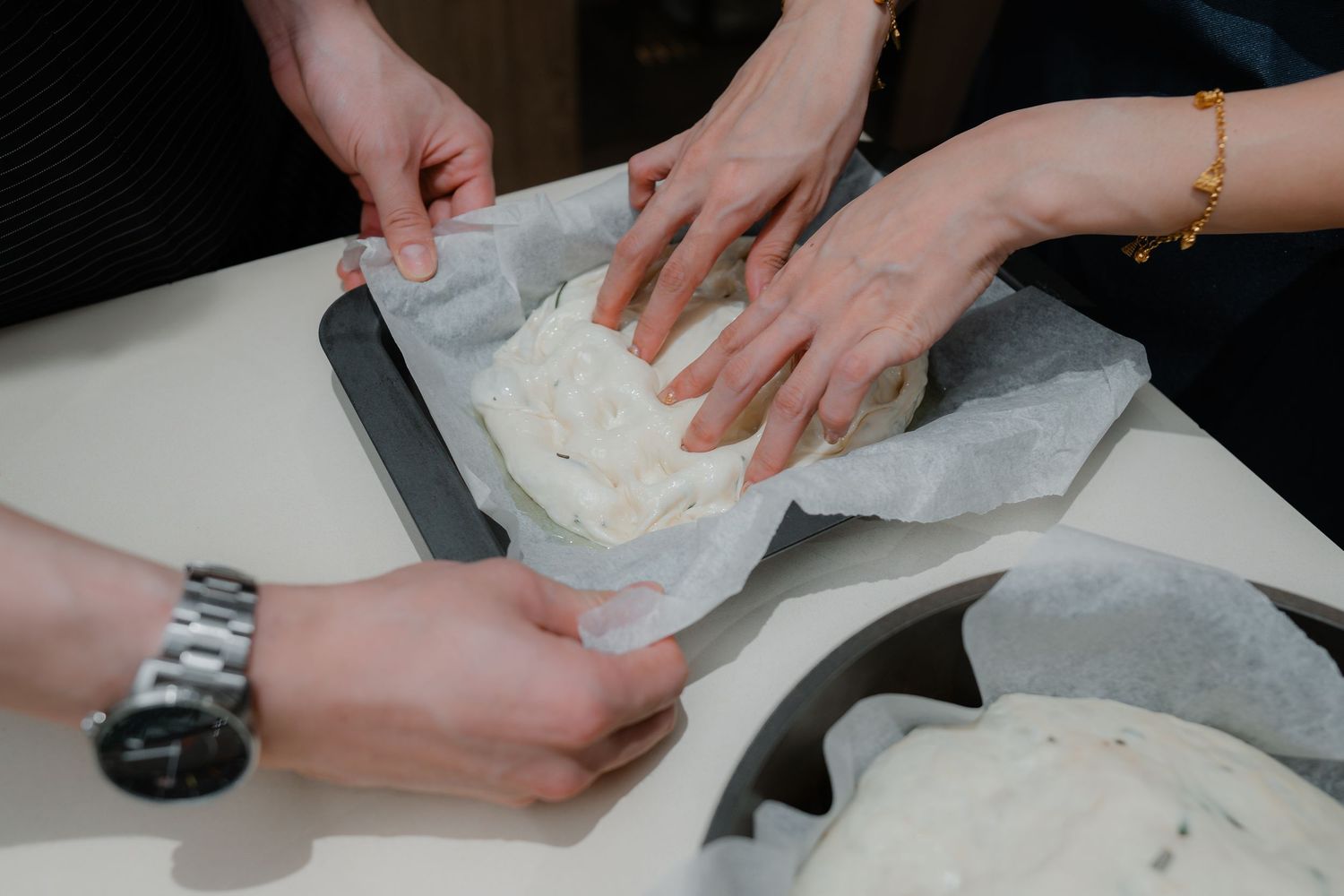 Hands preparing dough on a white surface with parchment paper.
