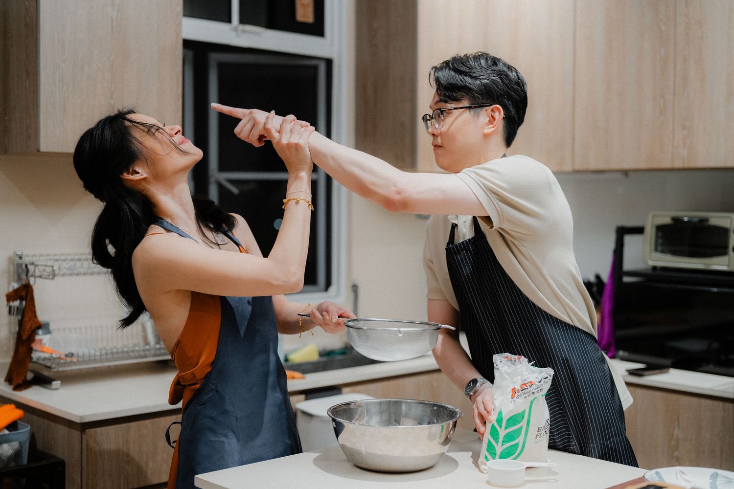 Two people playfully getting messy while baking together in a bright kitchen.