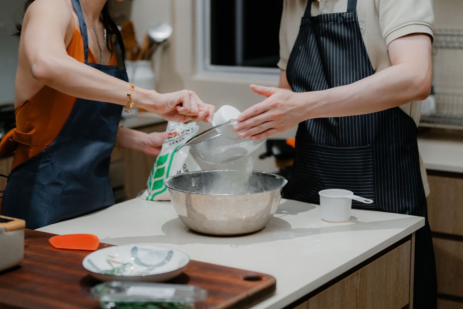 Hands working together to prepare ingredients in a mixing bowl on a kitchen counter.