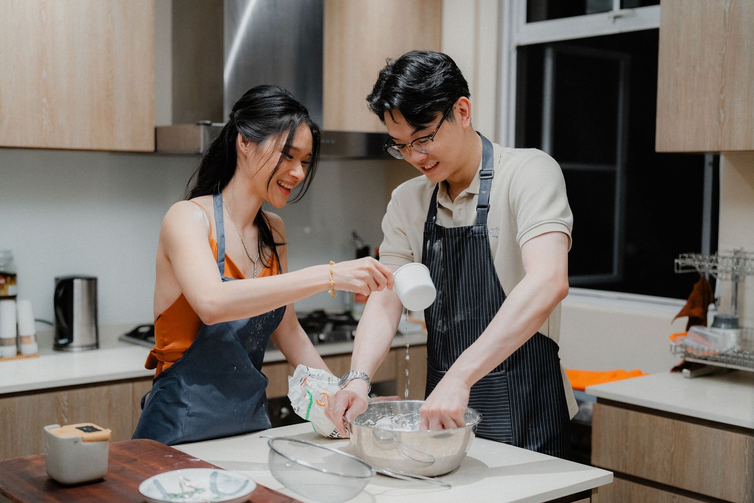 Couple kneading dough together on kitchen counter.