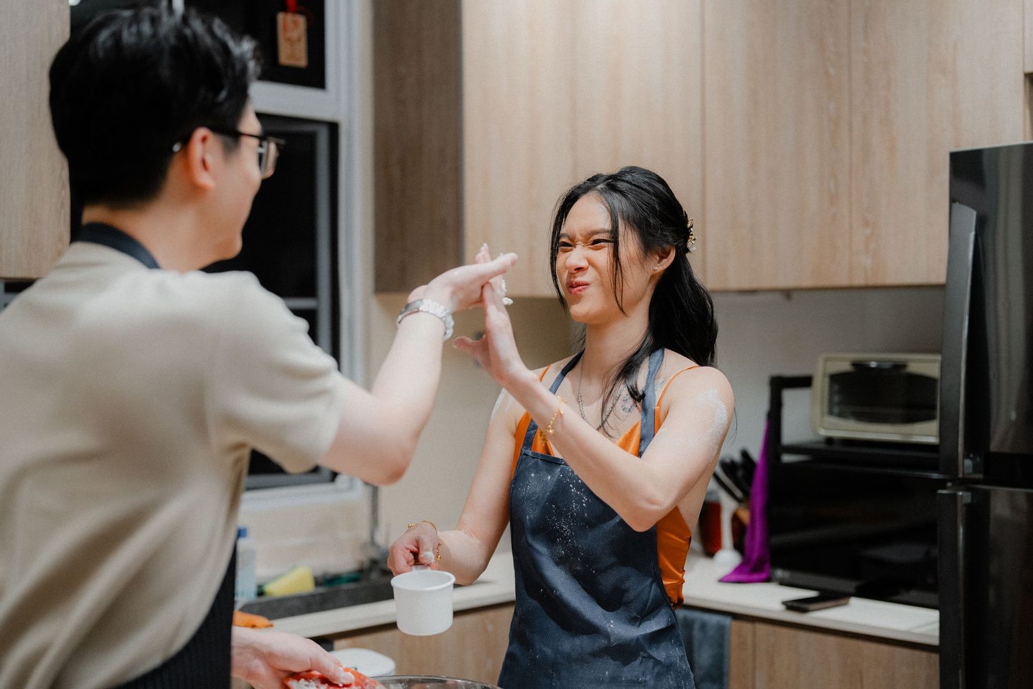 Playful flour fight between couple while baking in modern kitchen.