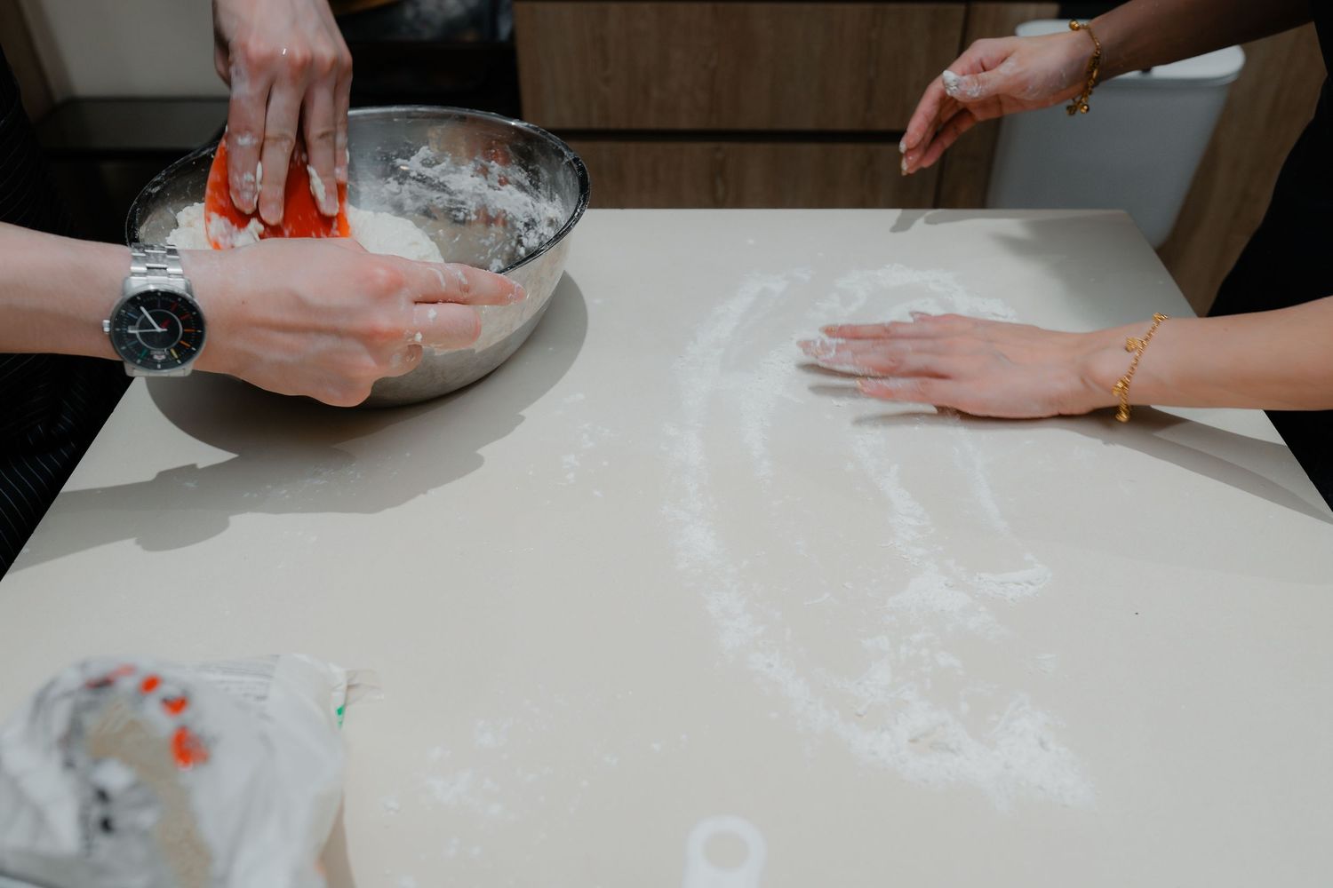 Hands working with flour and dough on a white countertop.