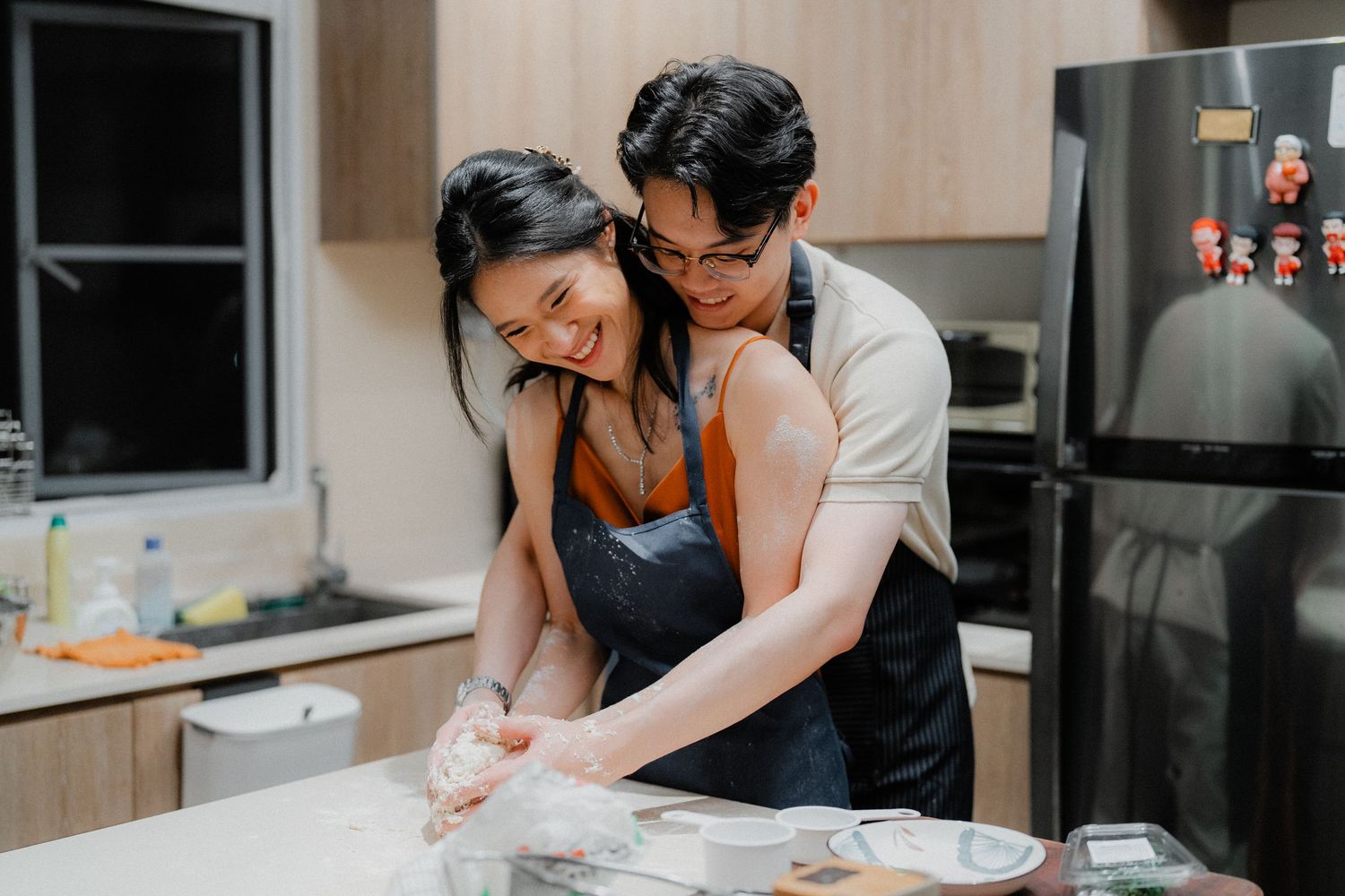 Two people baking together in a modern kitchen while kneading dough on a flour-dusted countertop.