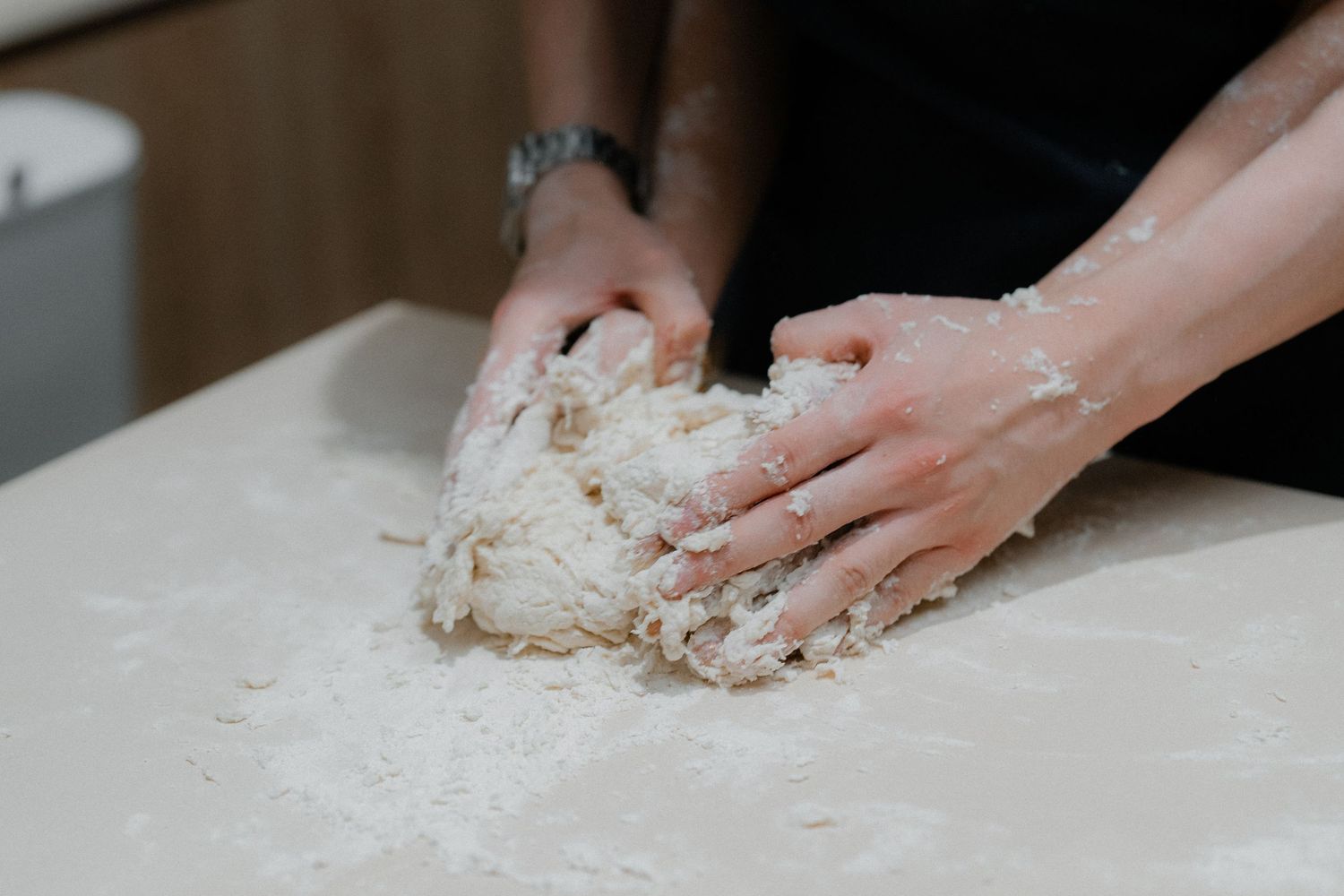 Close-up of hands kneading white dough on a floured surface.