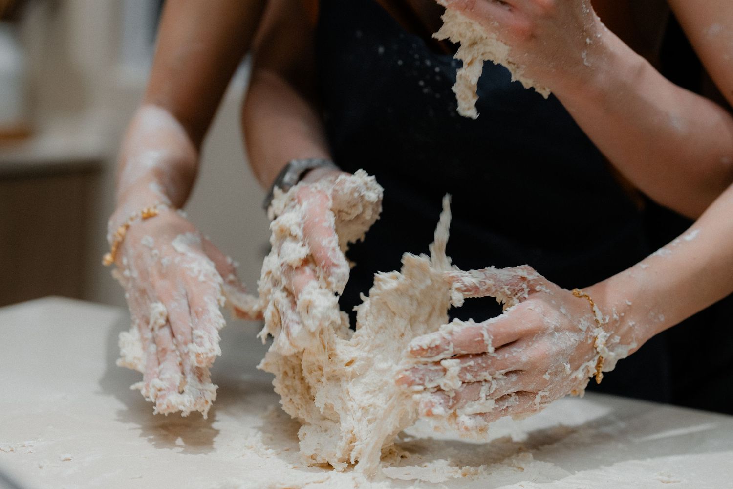 Close-up of hands covered in flour while kneading bread dough on white countertop.