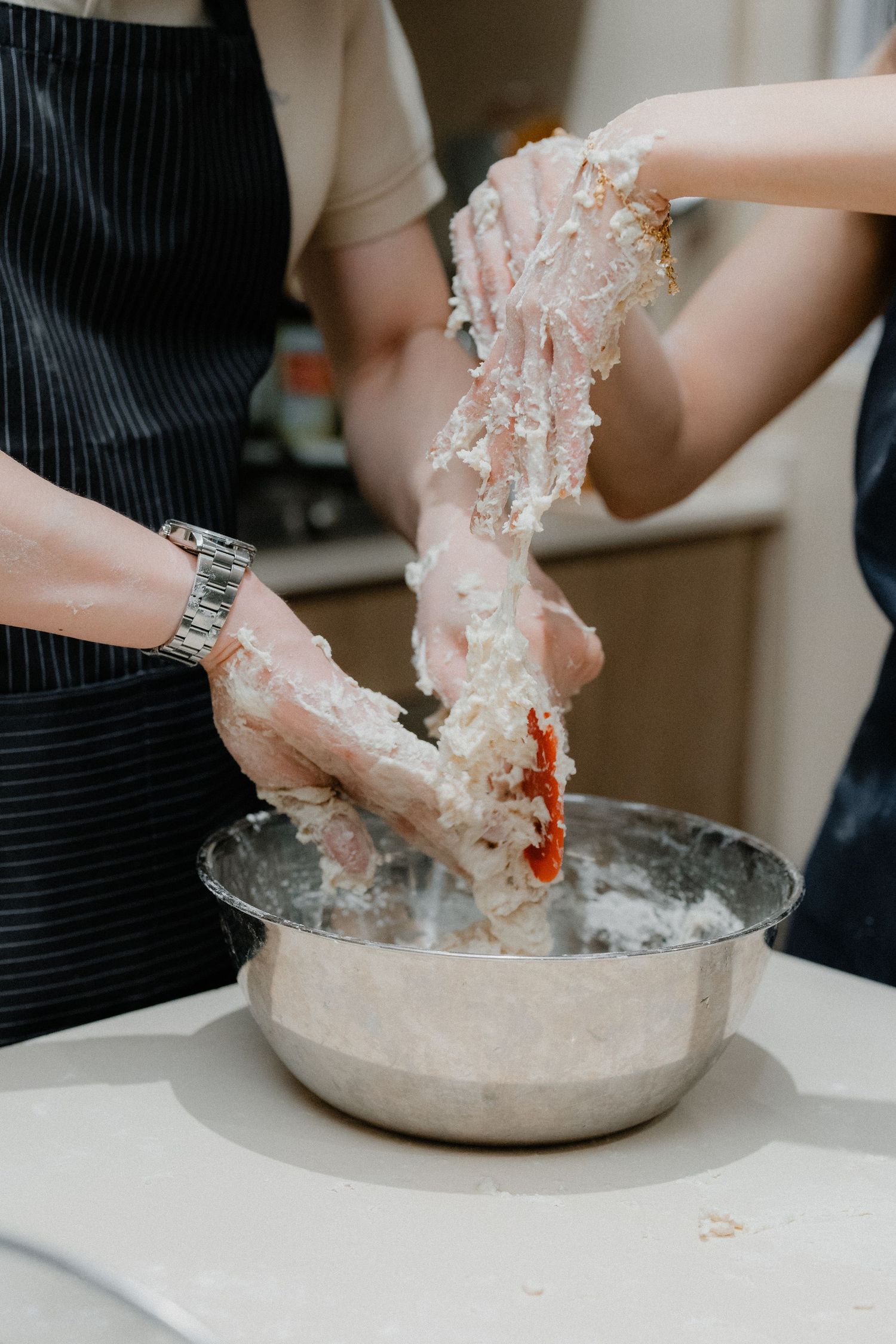 Hands kneading sticky dough mixture in a metal mixing bowl on white countertop.