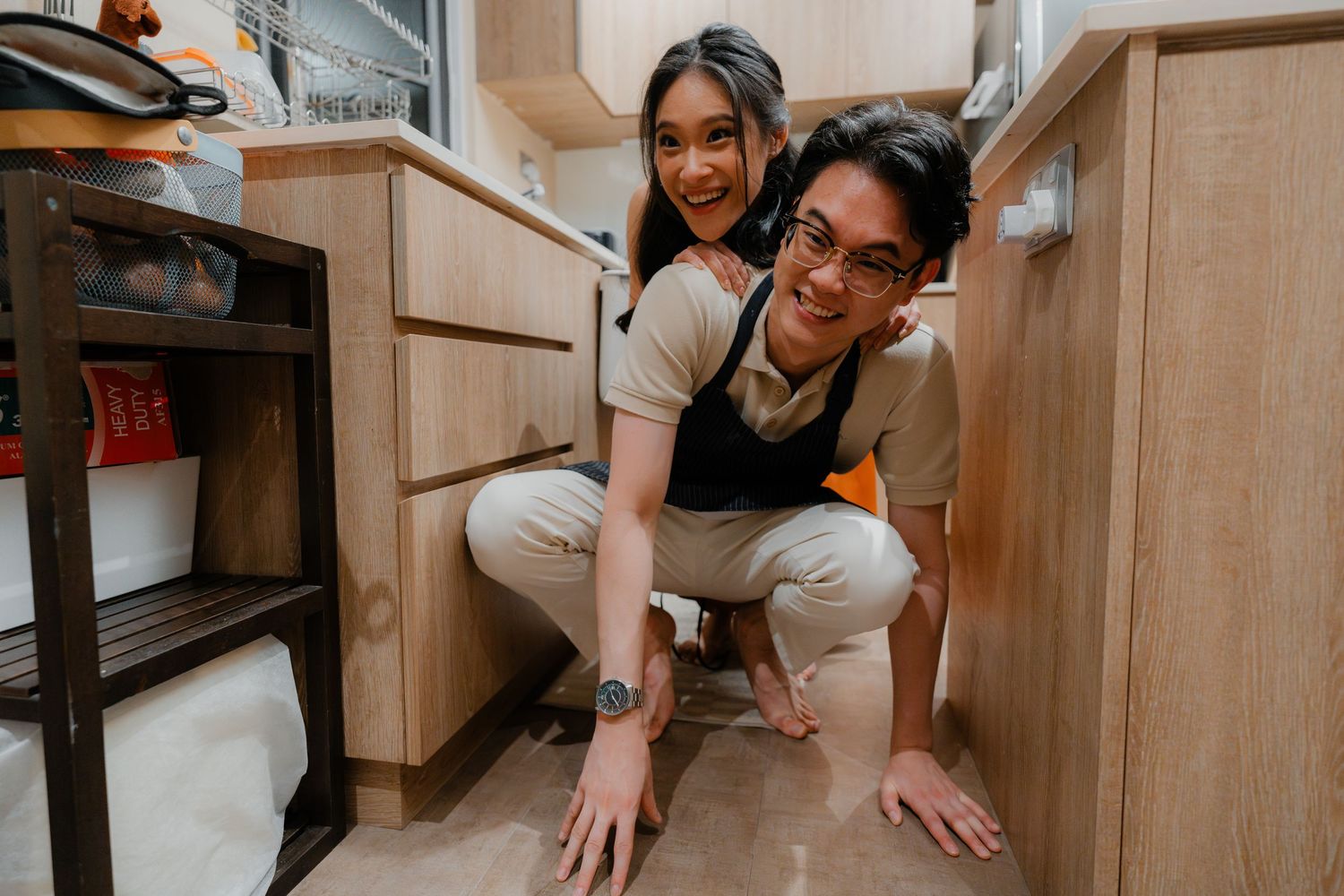 Two people having fun searching for something under kitchen cabinets together.