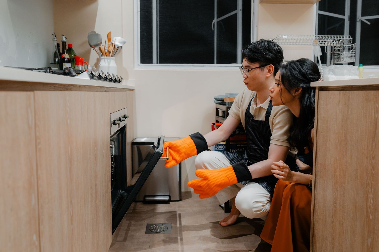 Two people crouching to check something in the oven while baking.