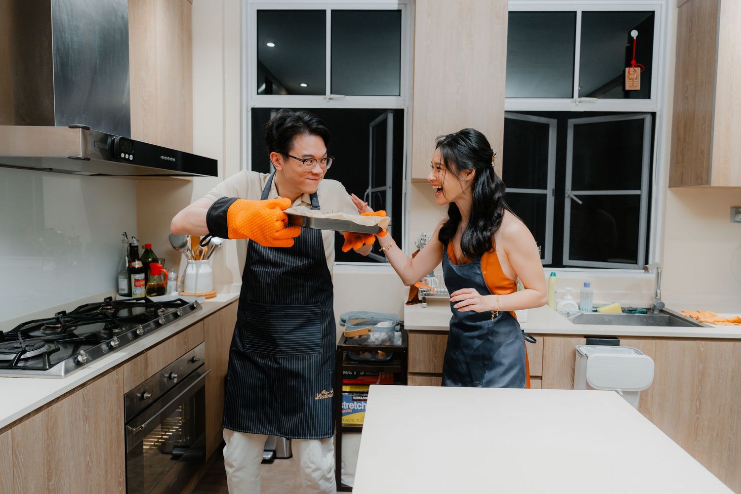 A couple in matching aprons playfully interacting while cooking in their modern kitchen.