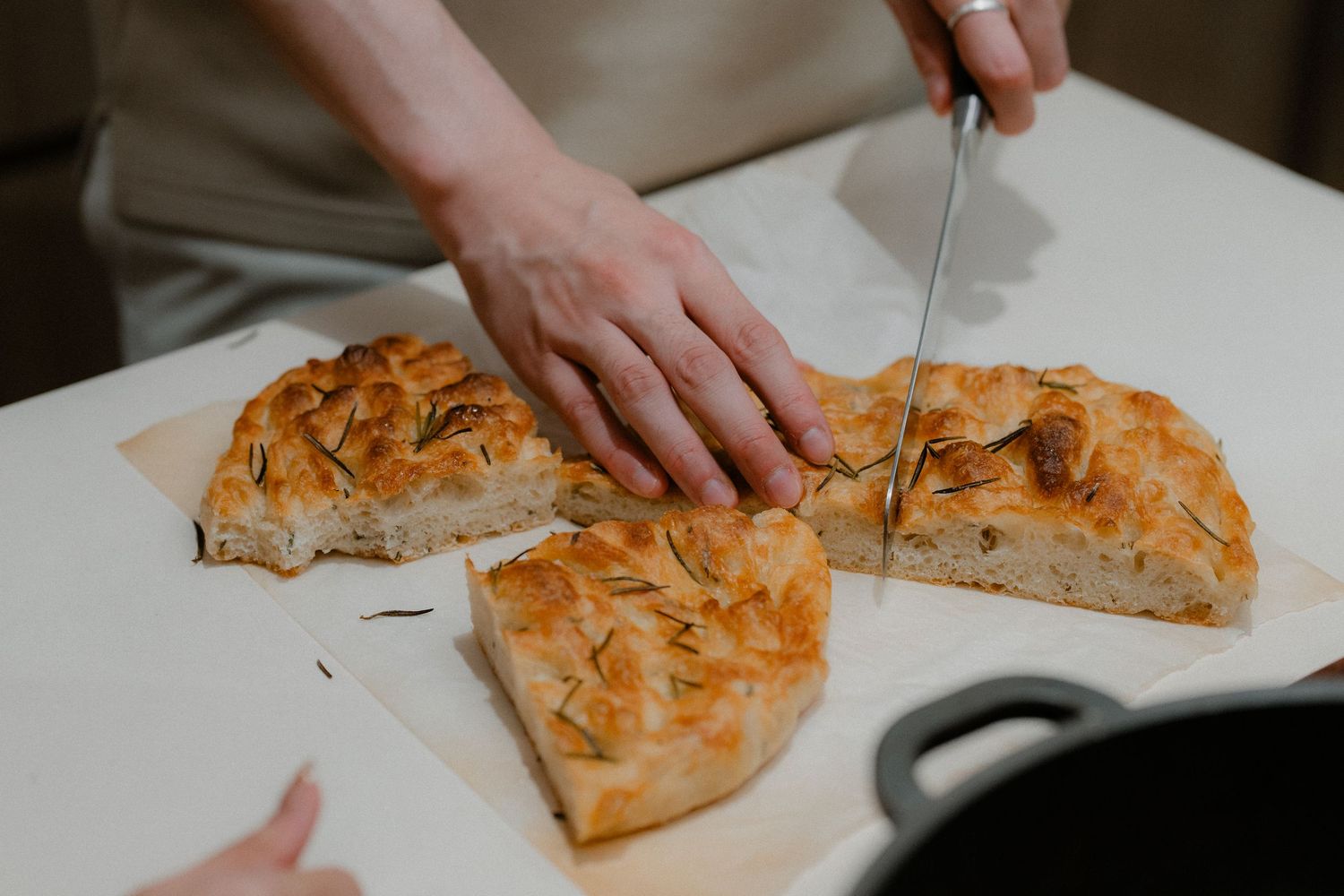 Hands cutting into golden brown flaky pastry on white cutting board in kitchen.