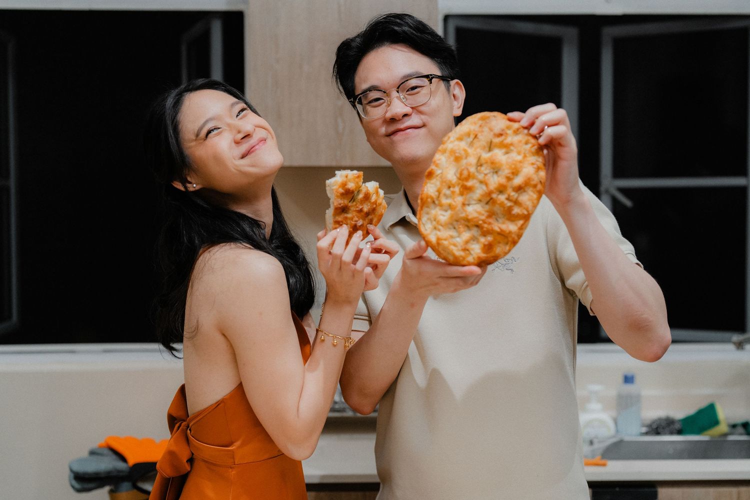 Couple showing off their heart-shaped pizza creation in the kitchen.