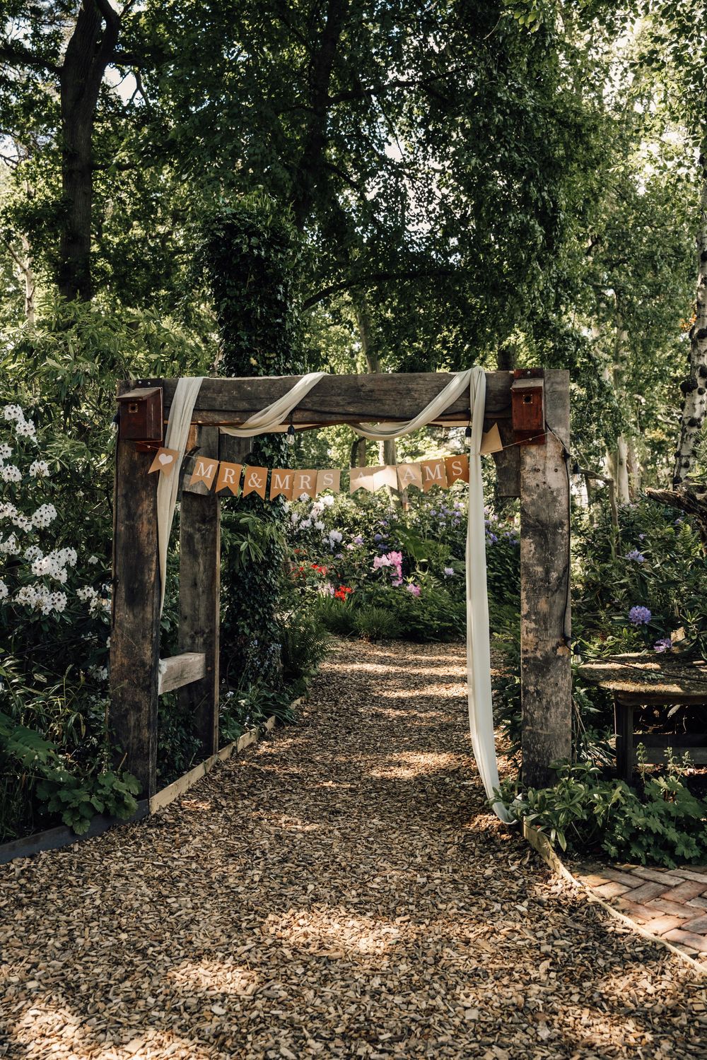 Natural wooded pathway decorated with wooden posts and hanging decorations for an outdoor event.