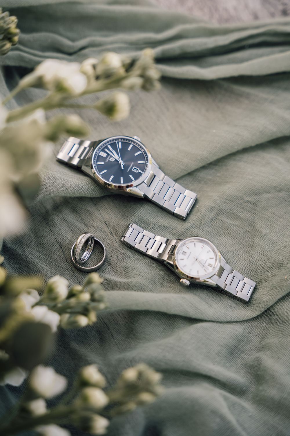 Silver watches and rings arranged on gray fabric with soft lighting.