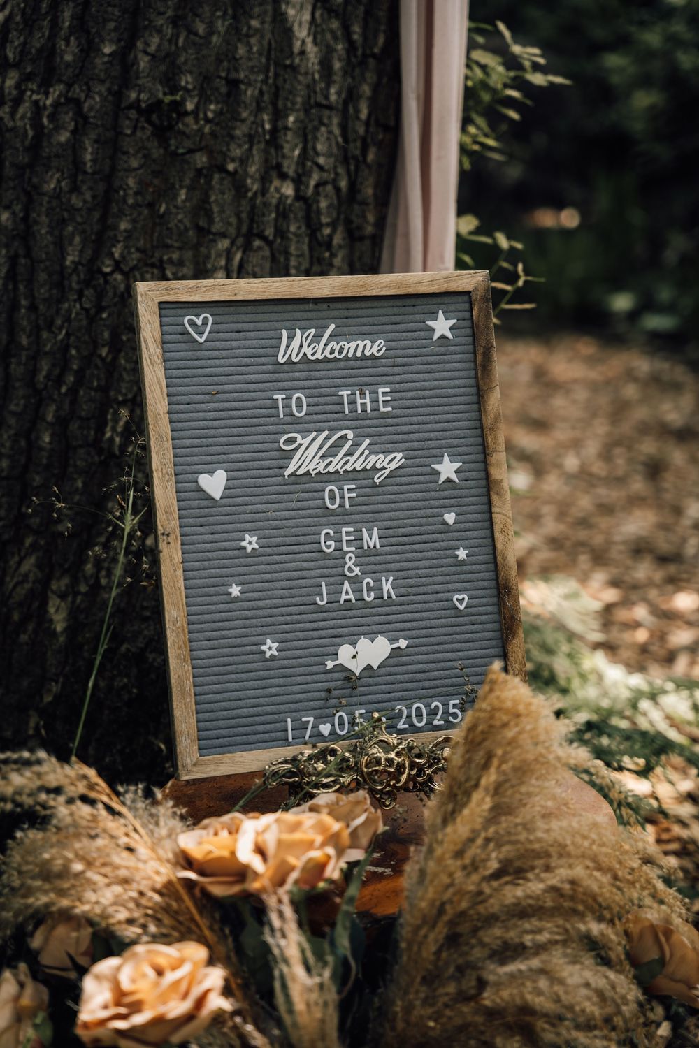 A letterboard wedding welcome sign displays the date and couple's names against a tree trunk.