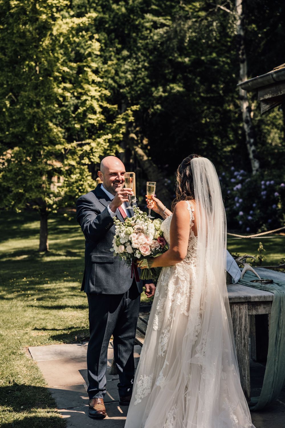 A first look moment between newlyweds on a sunny outdoor path surrounded by lush greenery.