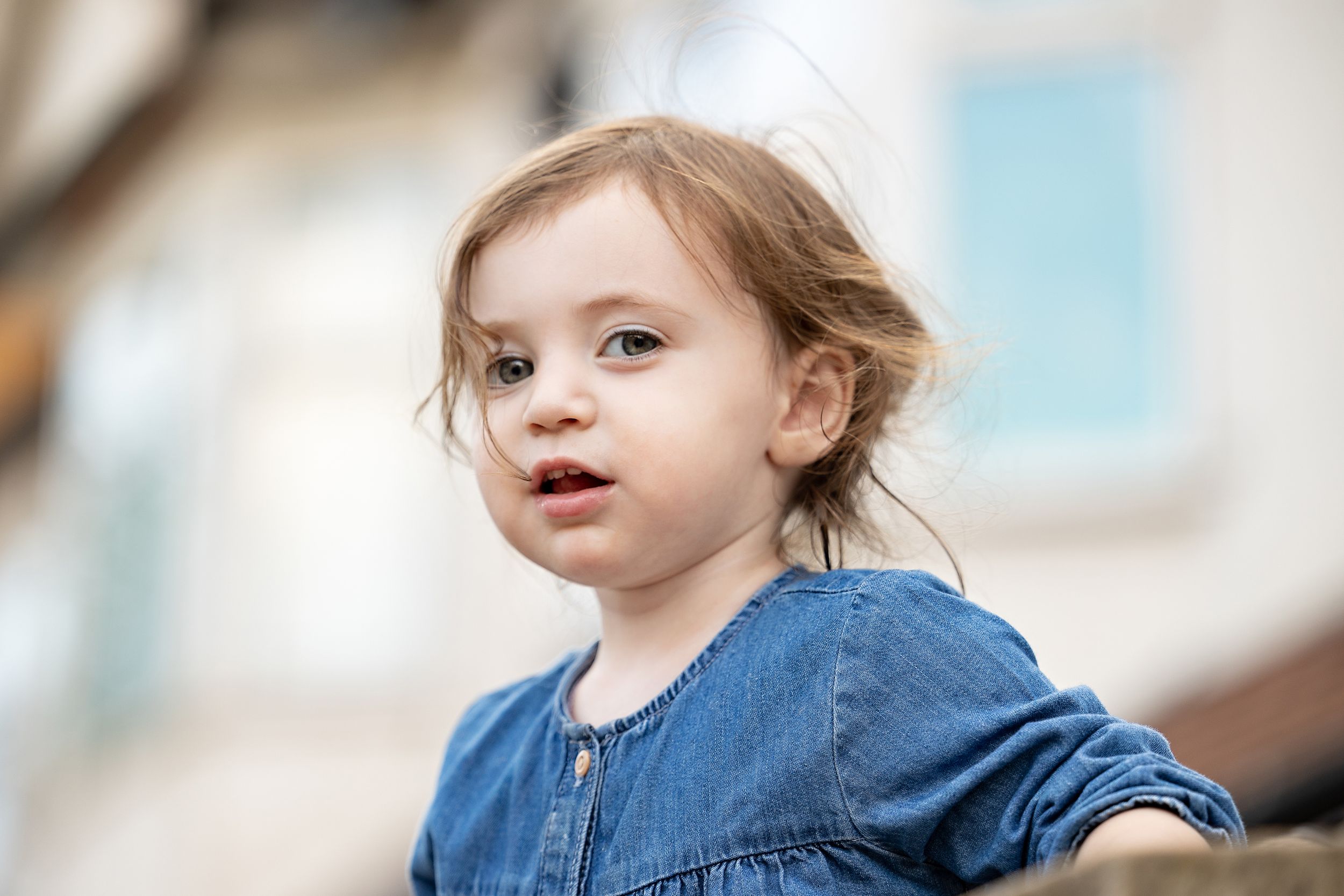 A child with blonde hair wearing a navy blue dress looking up with an expressive face outdoors.