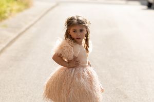 Young child wearing a light peach colored tulle party dress with short sleeves stands on an empty road.
