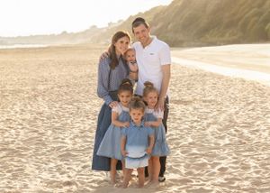Family portrait of a group in coordinated blue outfits standing together on a beach at sunset.