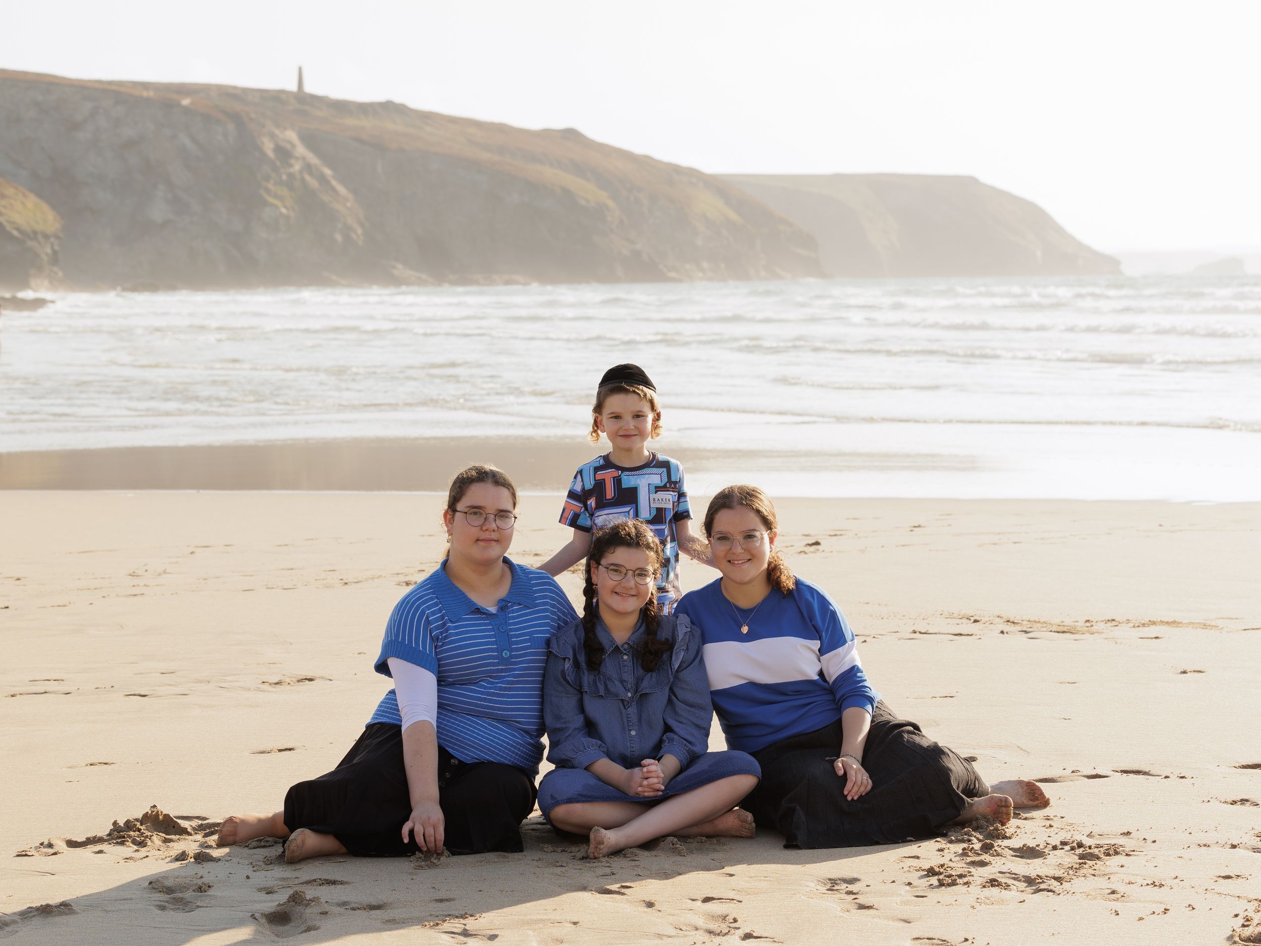 A group sits together on a sandy beach with coastal cliffs and ocean waves visible in the misty background.