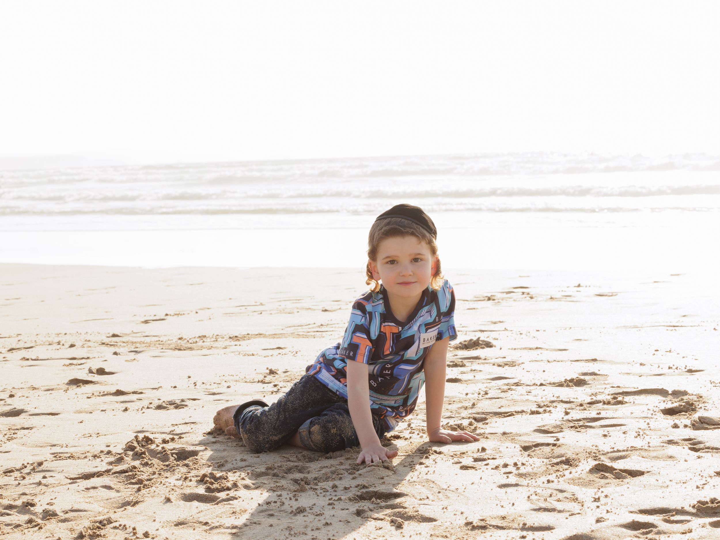A young person in plaid shirt plays in the sand on a sunny beach shore.