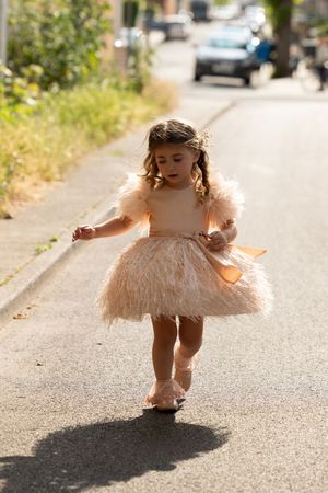 Small child twirling in a fluffy peach-colored dress on a sunny suburban street.