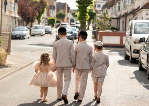 A group walking down a sunny residential street wearing coordinated beige outfits with a little girl in a tulle dress.