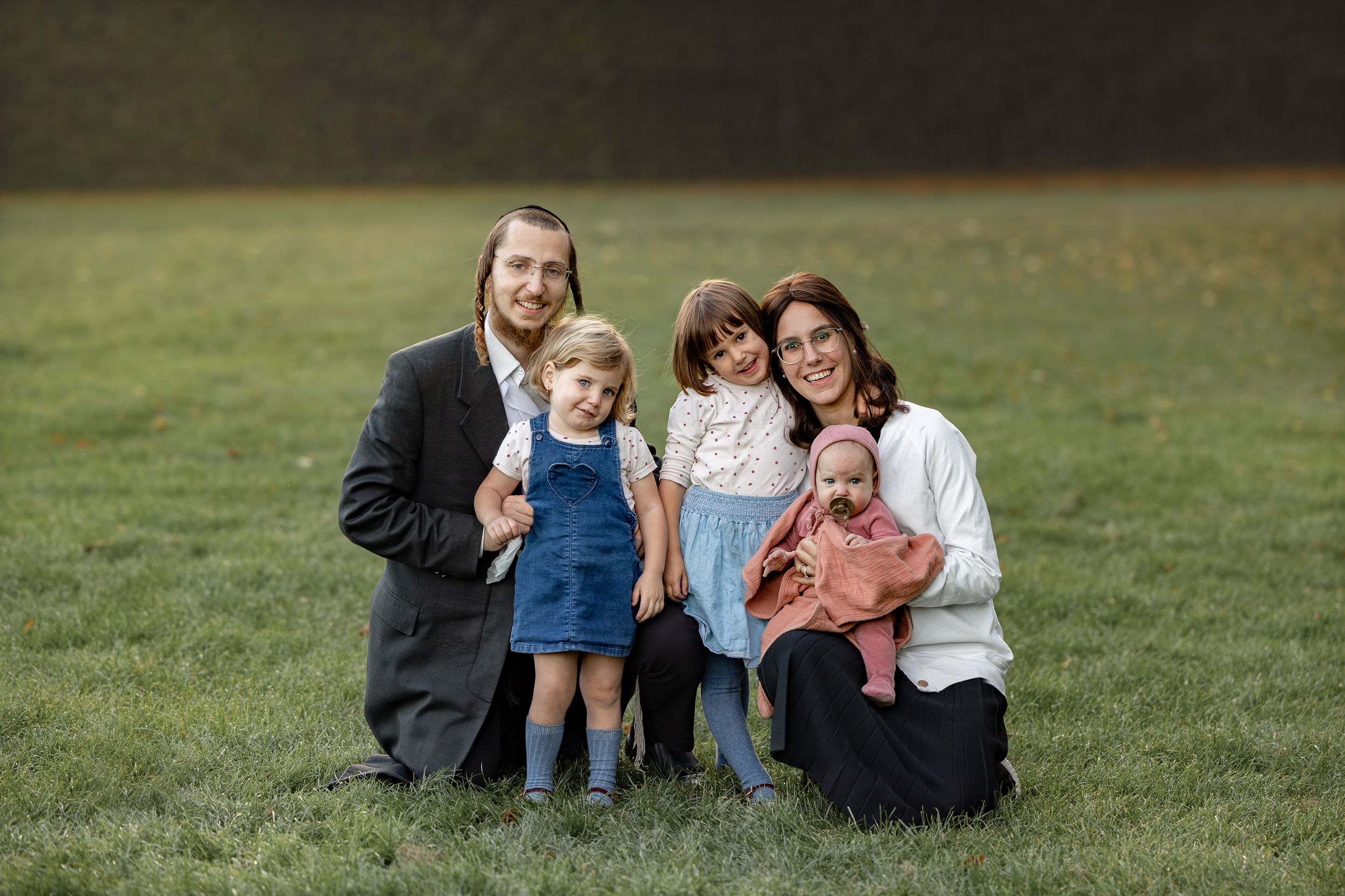 Family group sitting together on grass in casual outdoor portrait.