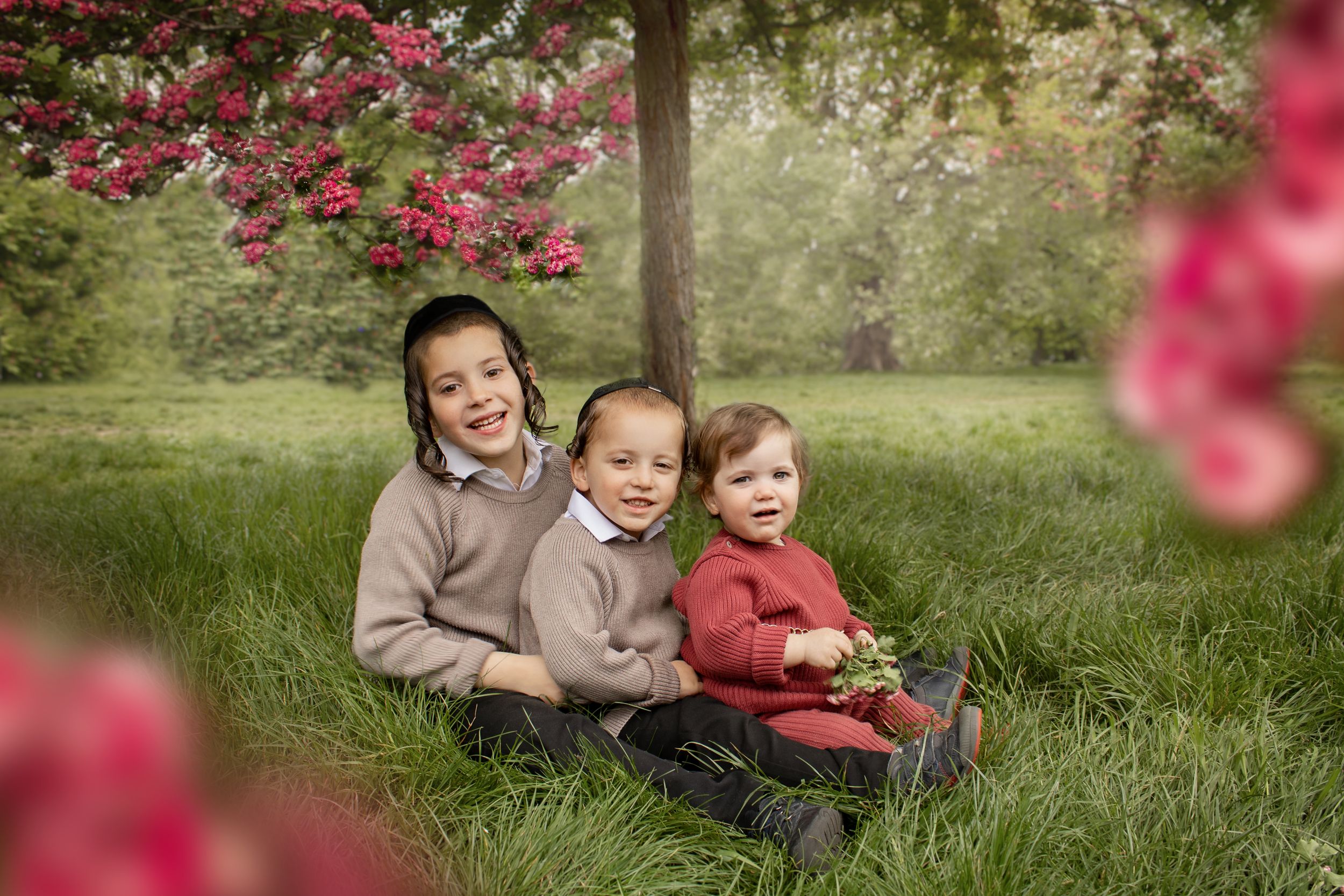 A sweet family moment captured under pink blossoming trees in a lush green field.