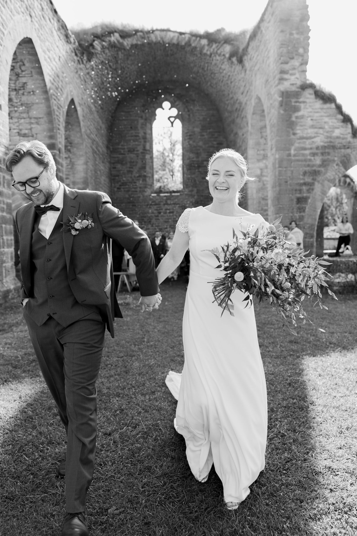 A joyful wedding moment captured in black and white at a historic stone church with Gothic arched windows.