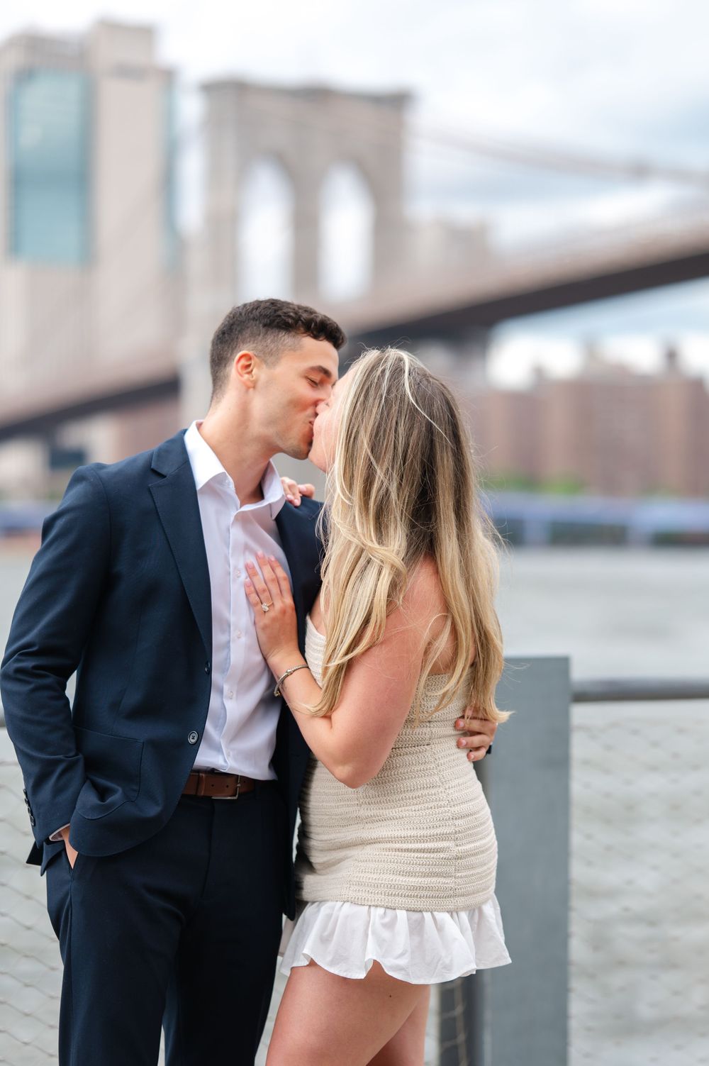 A couple shares a romantic moment in front of the Brooklyn Bridge on a cloudy day during their NYC proposal. Photo by Joliette Marie Photo.