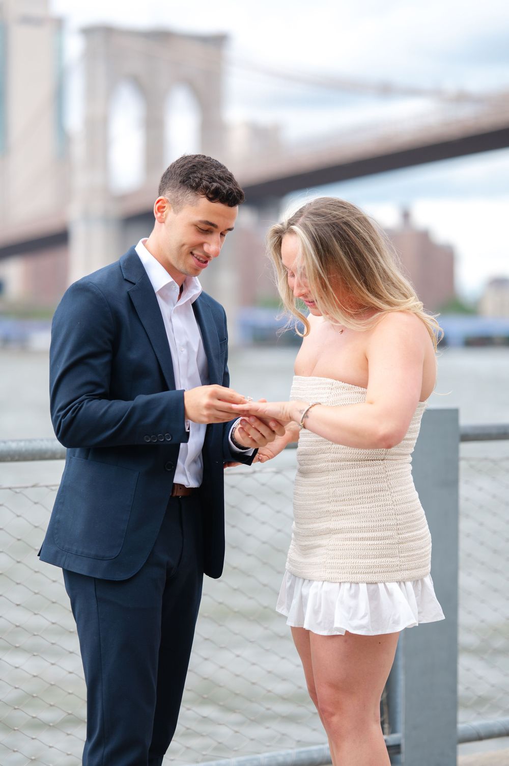 Proposal moment captured at Brooklyn Bridge Park as couple looks at engagement ring. NYC proposal captured by Joliette Marie Photography.