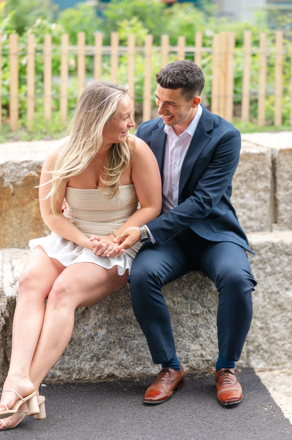 Newly engaged couple sharing an intimate moment while sitting on stone steps in a garden setting.