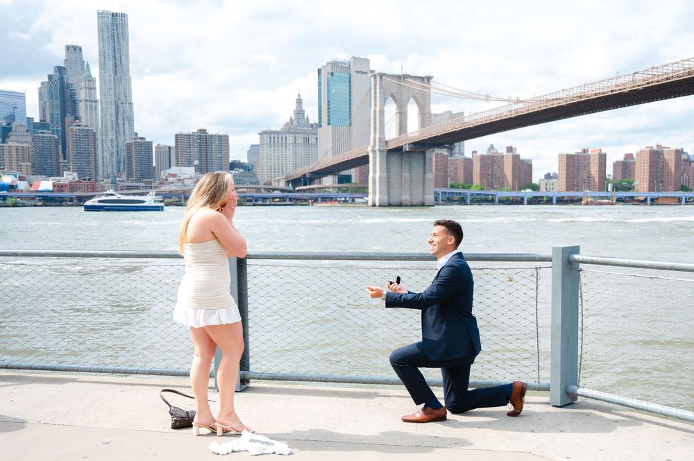 Person proposing on one knee by Brooklyn Bridge with Manhattan skyline backdrop and East River views caught by NYC proposal photographer.