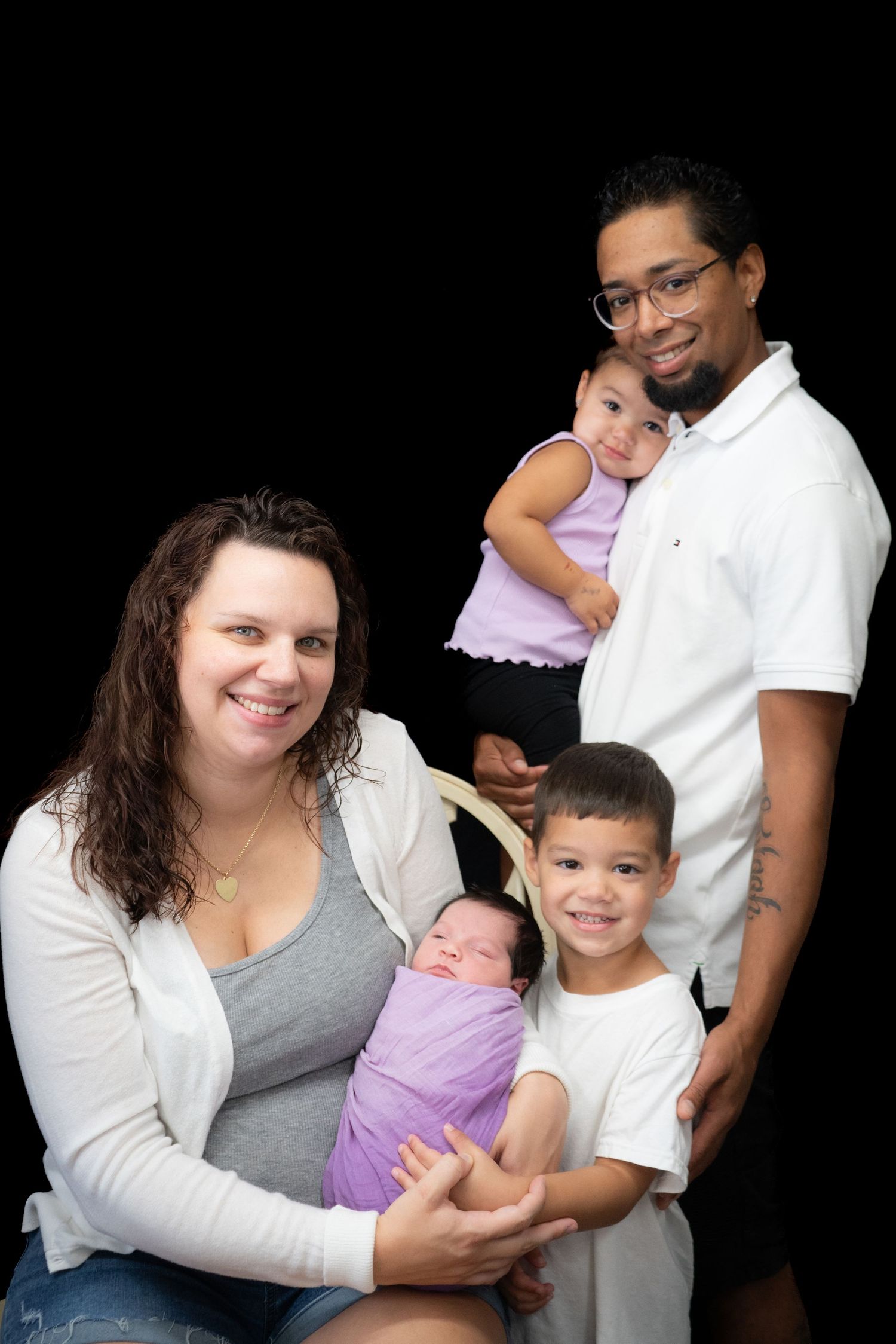 Portrait of multi-ethnic family with three children against black backdrop.