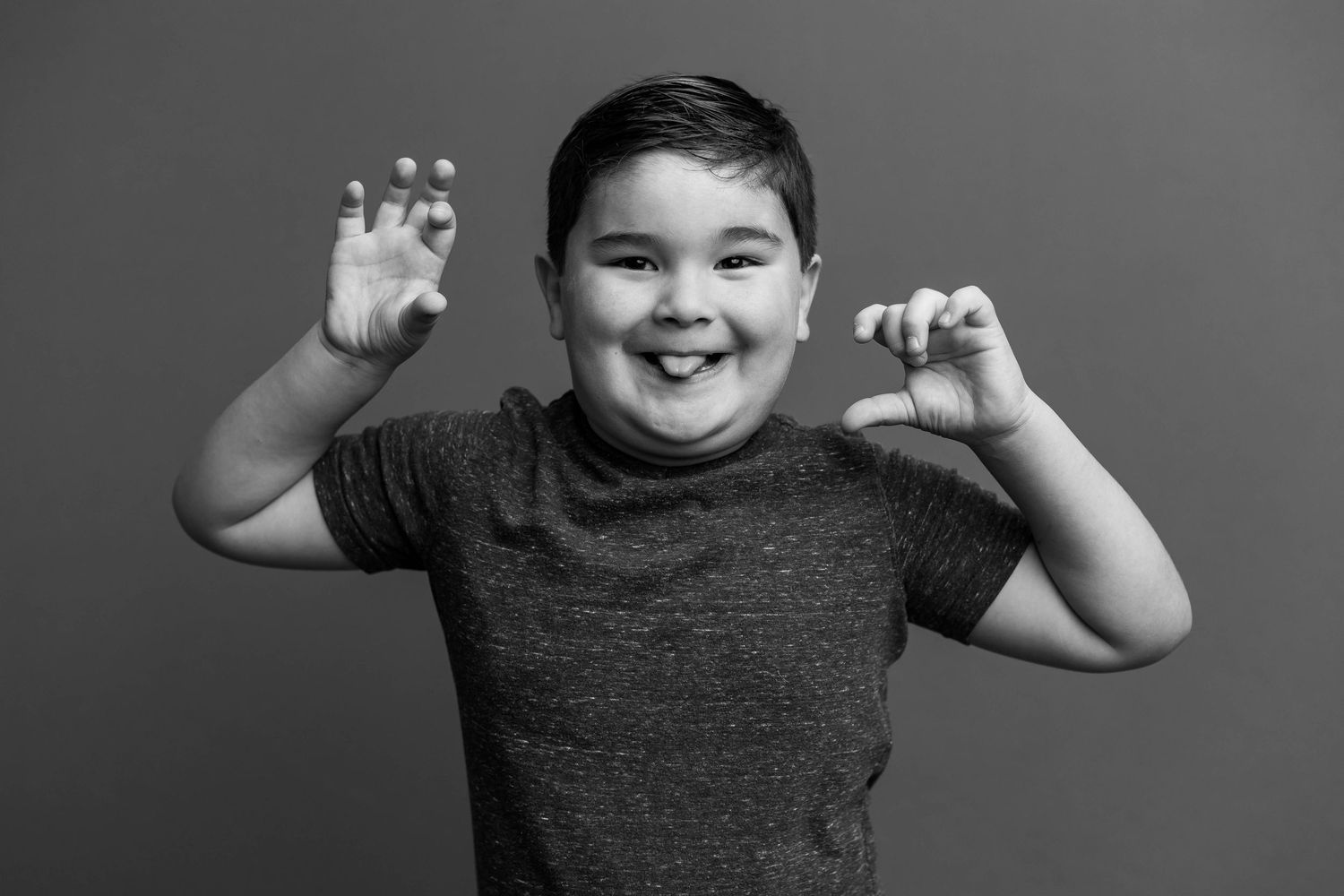 Black and white portrait of a playful child wearing a dark t-shirt while making claw hands and a silly expression.