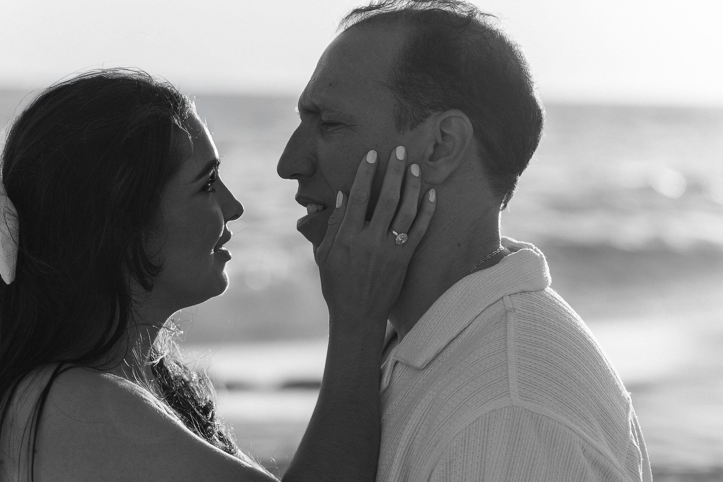 Black and white portrait of a couple sharing a romantic moment by the ocean.