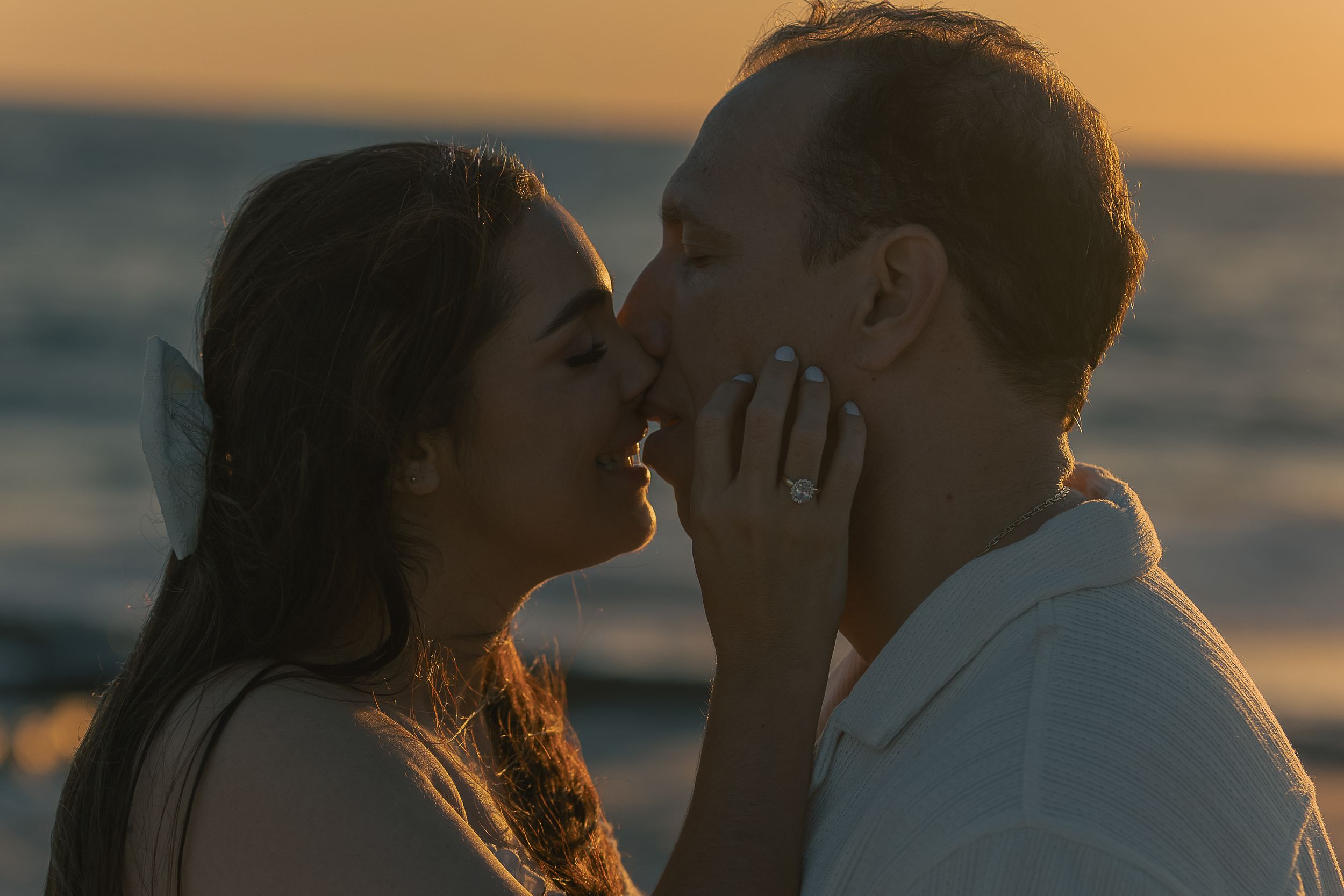 A couple embraces against a warm sunset sky during their beach photoshoot.