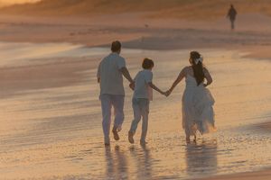 Three figures walking together along a sandy beach during golden hour.