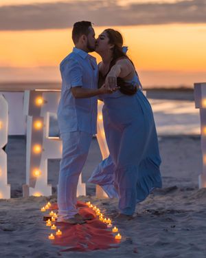 Romantic couple embraces on beach at sunset with glowing candles in the sand creating an intimate atmosphere.