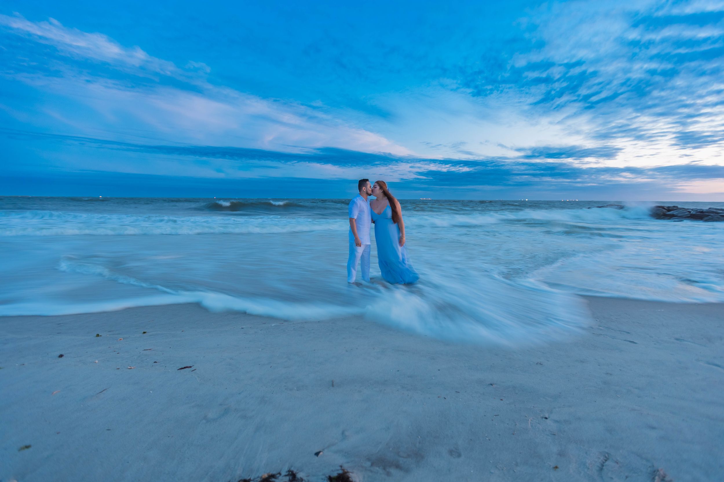 People walking along a scenic beach shoreline at sunset with waves crashing and blue skies overhead.