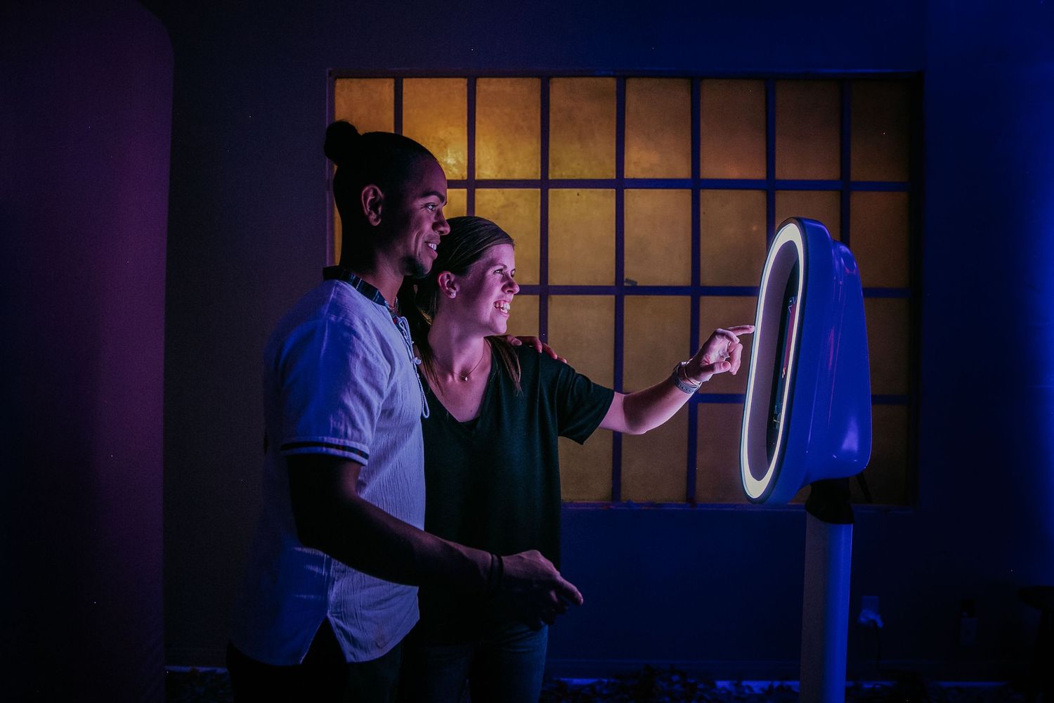 Two people stand in a dark room gazing at a glowing round LED screen with blue lighting in the background.