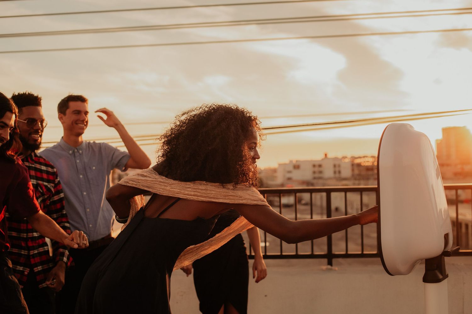 People dance together on a rooftop balcony during sunset in a city, with golden light illuminating the scene.