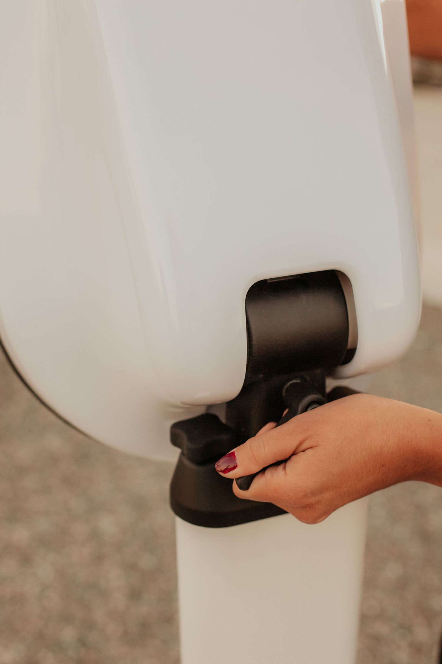 A hand with painted nails operates a white water dispenser or beverage container with a black spout.