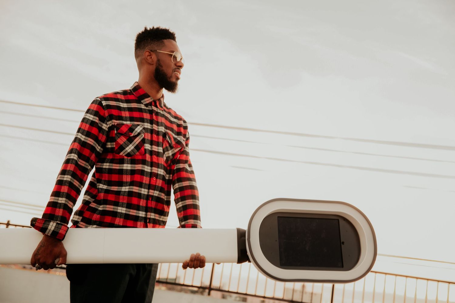 Person in red plaid flannel shirt looking away from camera on urban rooftop with white camera equipment.