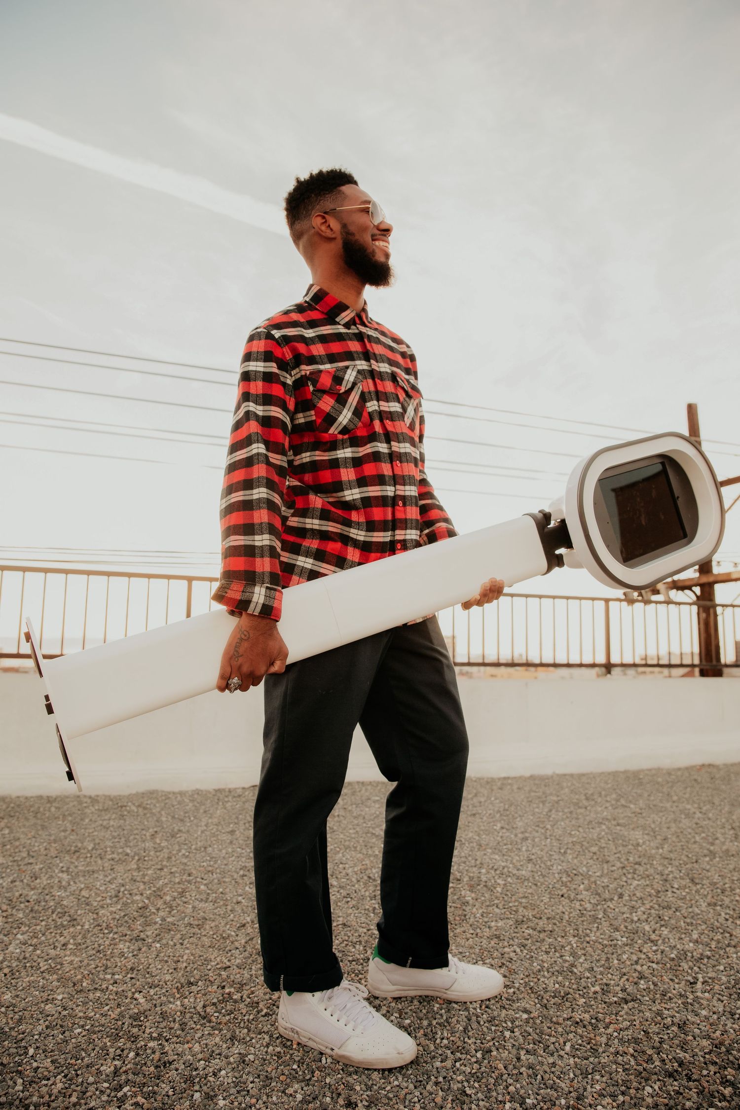 Person in red plaid flannel shirt and black pants carrying white surfboard on cloudy day.