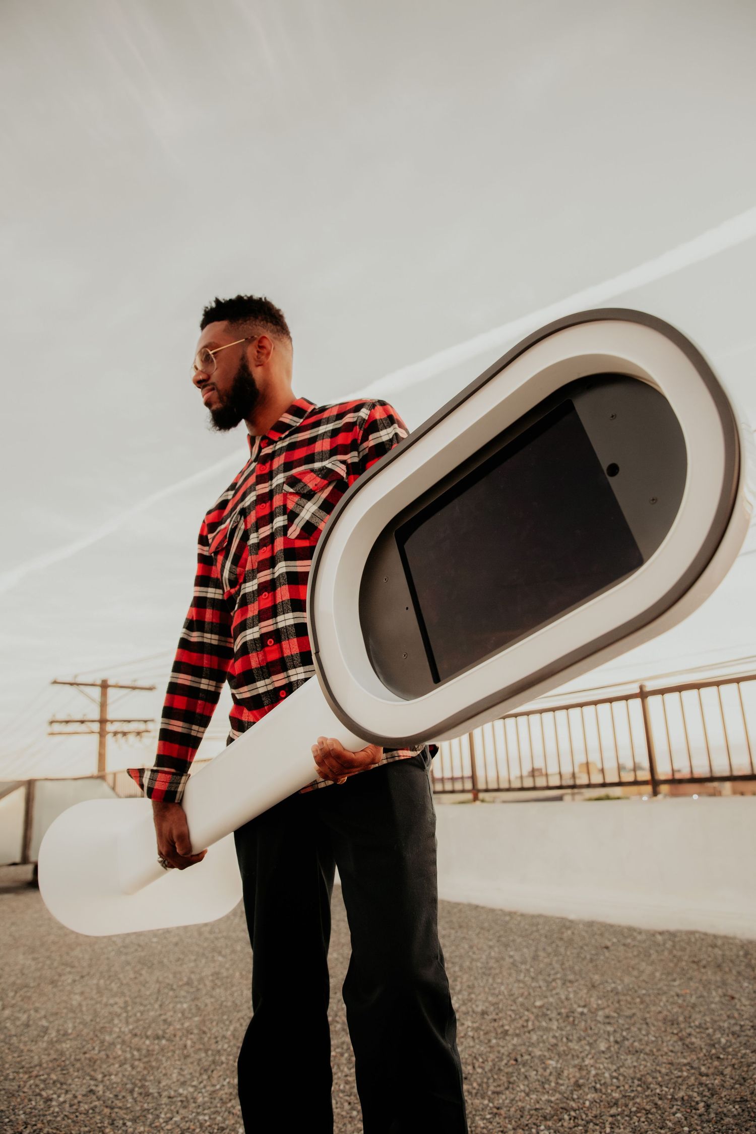 A person in a plaid shirt holds a large oval-shaped display panel against an overcast sky.