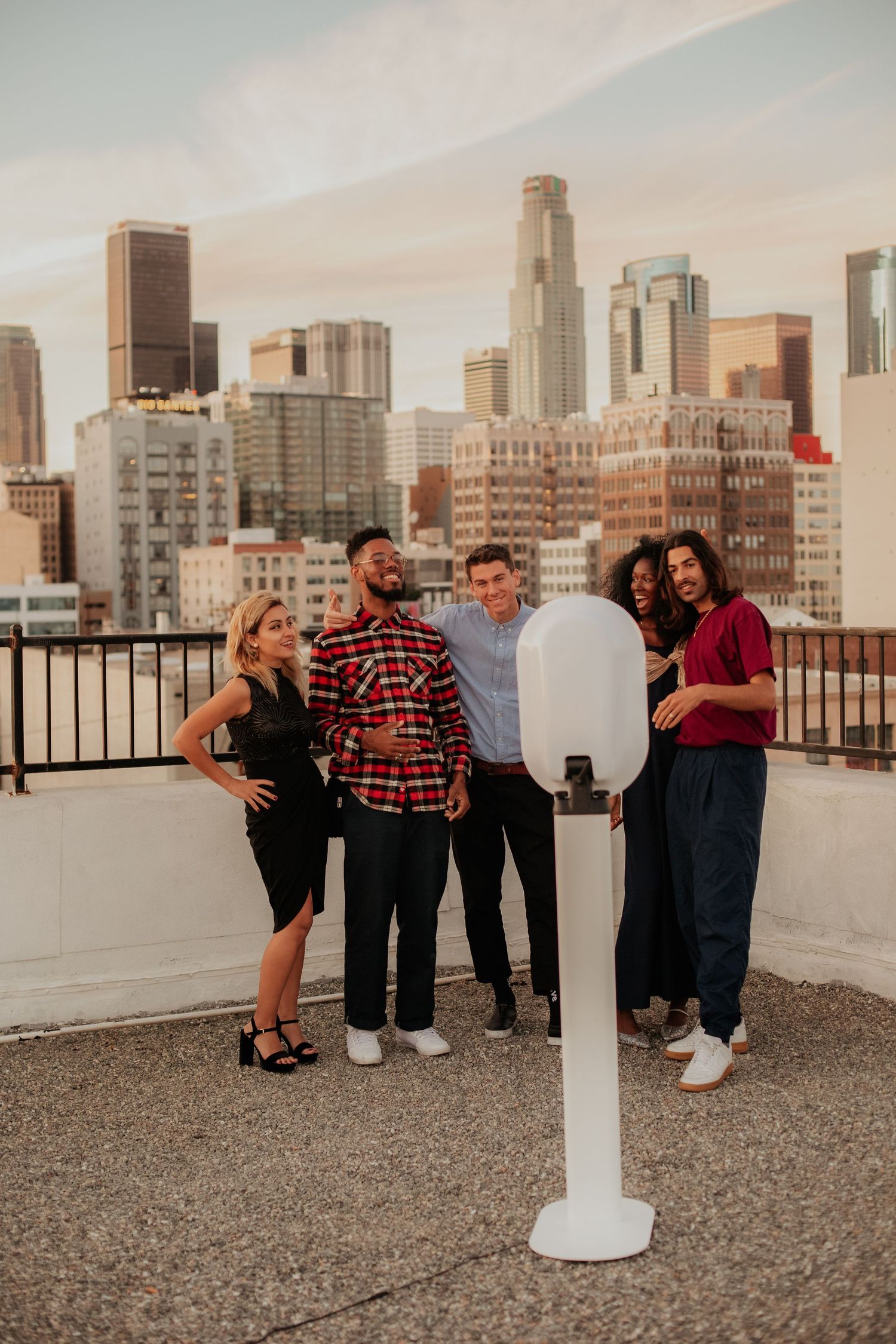 People gathered on a rooftop with Los Angeles downtown skyline at sunset with tall buildings in background.