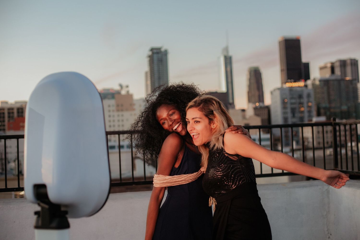 Two friends dancing and embracing on rooftop with city skyline at sunset.
